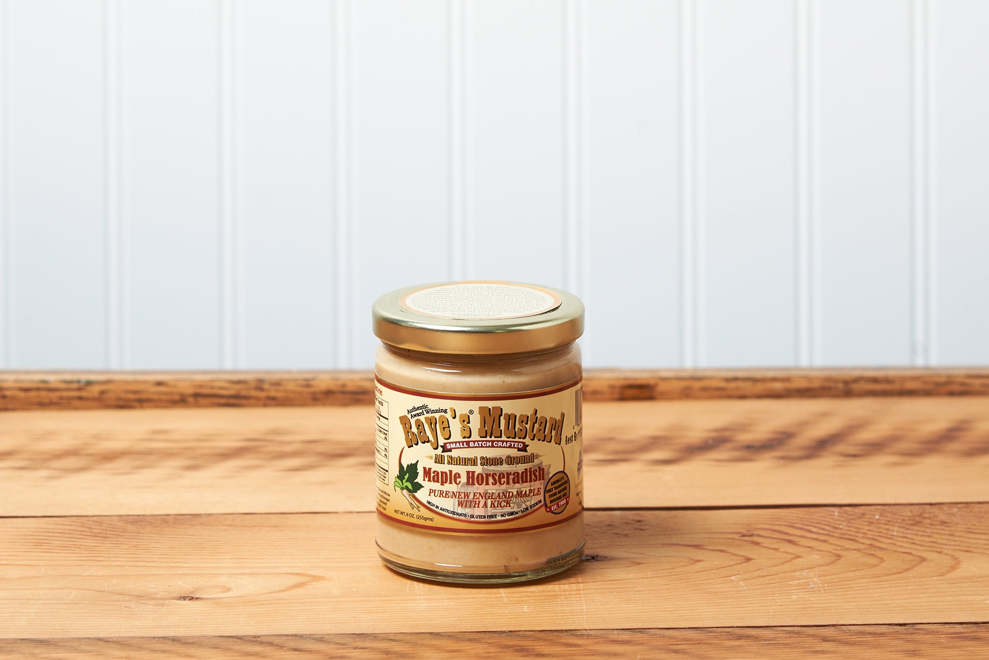 A jar of Raye's Maple Horseradish Mustard sits on a brown wooden table.