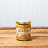 A jar of Raye's Top Dog Mustard sits on a brown wooden table.