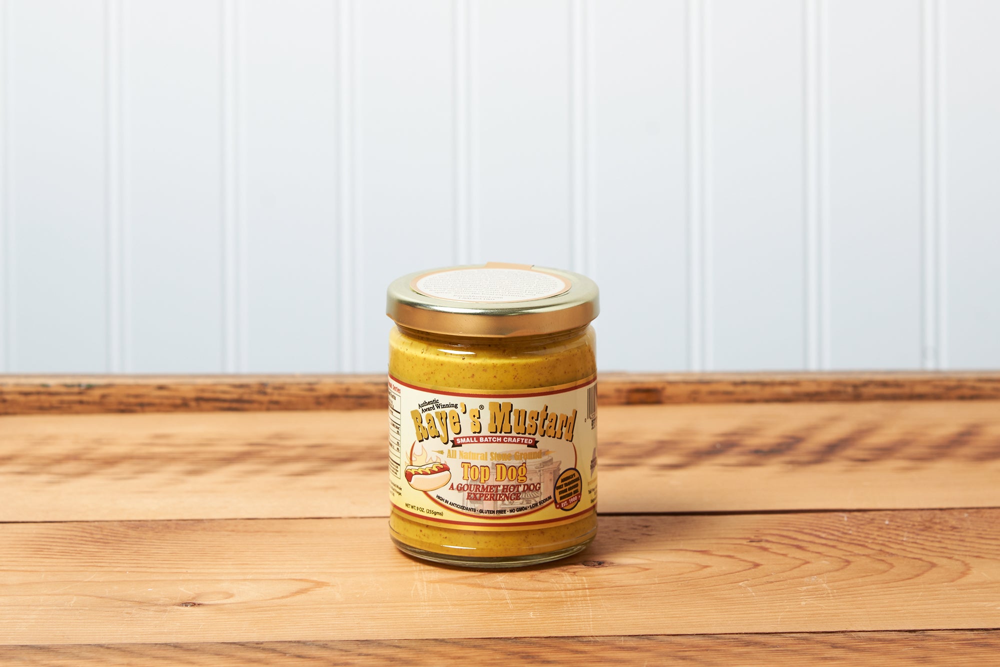 A jar of Raye's Top Dog Mustard sits on a brown wooden table.