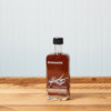 A bottle Runamok Cinnamon and Vanilla Infused Maple Syrup sits on a wooden tabletop.