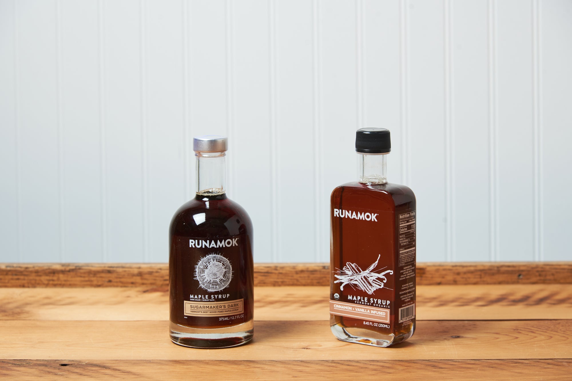 Two bottles of Runamok Maple Syrup sit on a wooden tabletop.