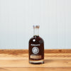 A bottle Runamok Sugarmaker's Dark: Wood-Fired Vermont Maple Syrup sits on a wooden tabletop.