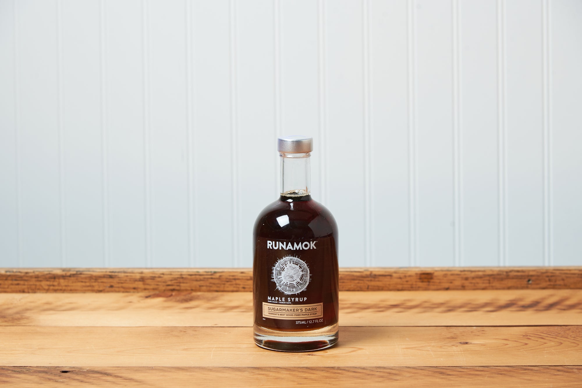A bottle Runamok Sugarmaker's Dark: Wood-Fired Vermont Maple Syrup sits on a wooden tabletop.