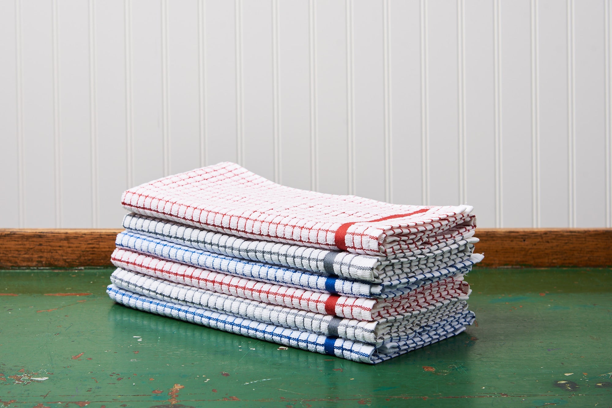 A stack of different color Samuel Lamont Poli-Dry Towels sit on a green wooden tabletop.