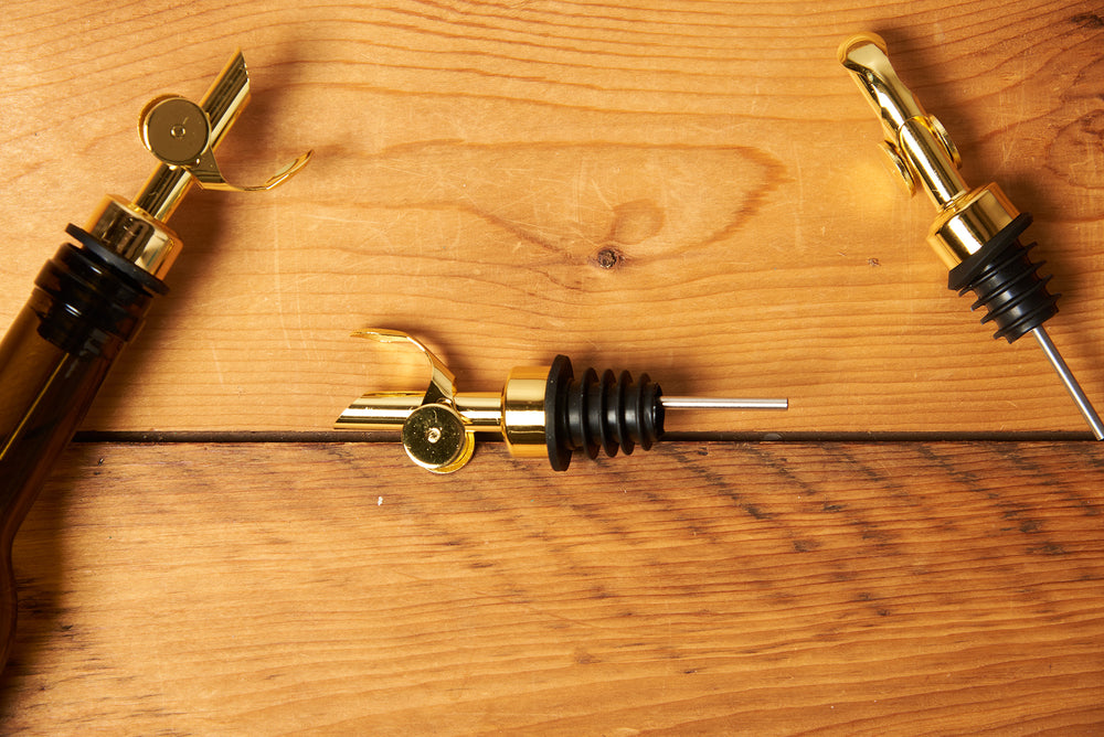 Gold Self Closing Weighted Pour Spouts sit on a wooden table.