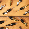 Many Self Closing Weighted Pour Spouts are scattered across a wooden table.