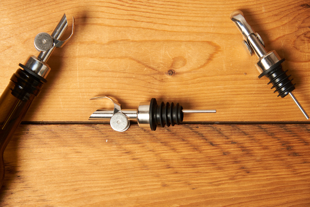 Silver Self Closing Weighted Pour Spouts sit on a wooden table.