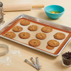 Freshly baked chocolate chips rest on a Mrs. Anderson's Half Size Silicone Baking Mat in a sheetpan. Baking tools surround the pan.
