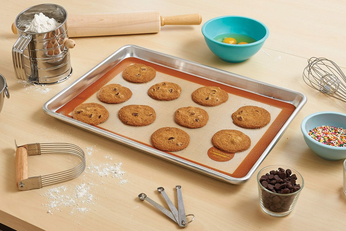 Freshly baked chocolate chips rest on a Mrs. Anderson's Half Size Silicone Baking Mat in a sheetpan. Baking tools surround the pan.