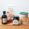 An assortment of Stonewall Kitchen items sit on a brown wooden table. The assortment includes: Wild Maine Blueberry Jam, Wild Maine Blueberry Syrup, Blueberry Scone Mix, and Farmhouse Pancake & Waffle Mix