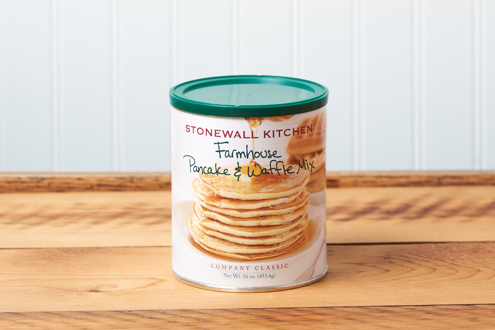 A canister of Stonewall Kitchen Farmhouse Pancake & Waffle Mix sits on a brown wooden table.