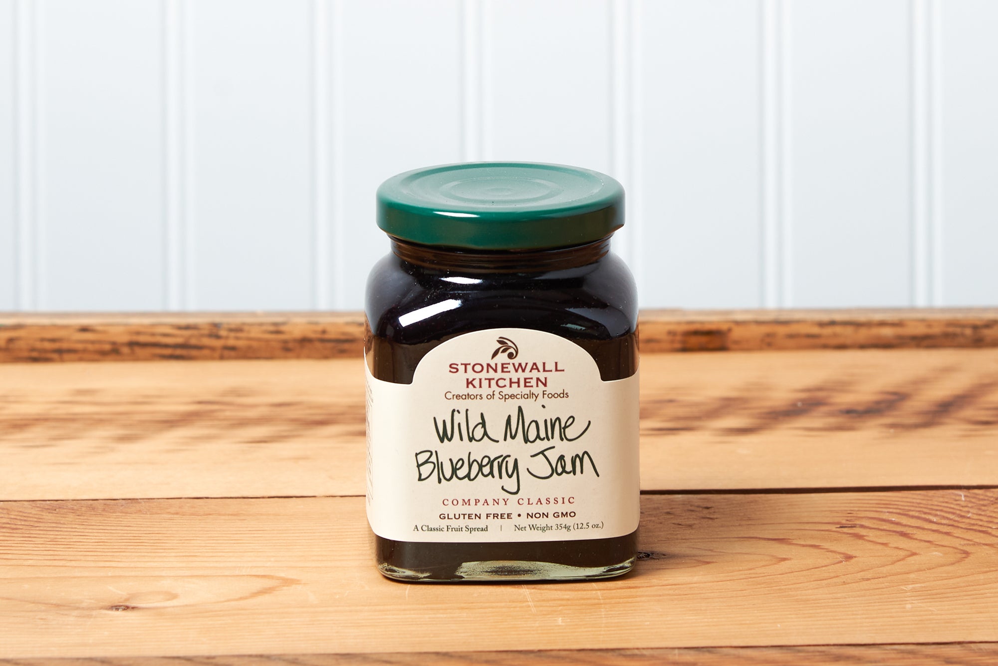 A jar of Stonewall Kitchen Wild Maine Blueberry Jam sits on a brown wooden table.