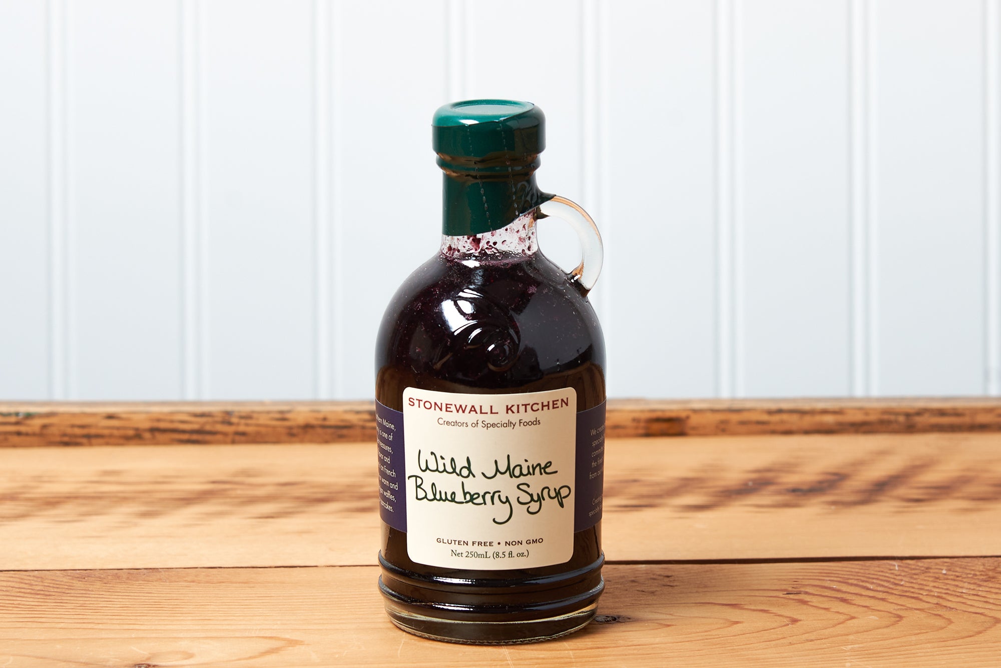 A bottle of Stonewall Kitchen Wild Maine Blueberry Syrup sits on a brown wooden table.