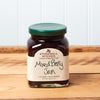 A jar of Stonewall Kitchen Mixed Berry Jam sits on a brown wooden table.