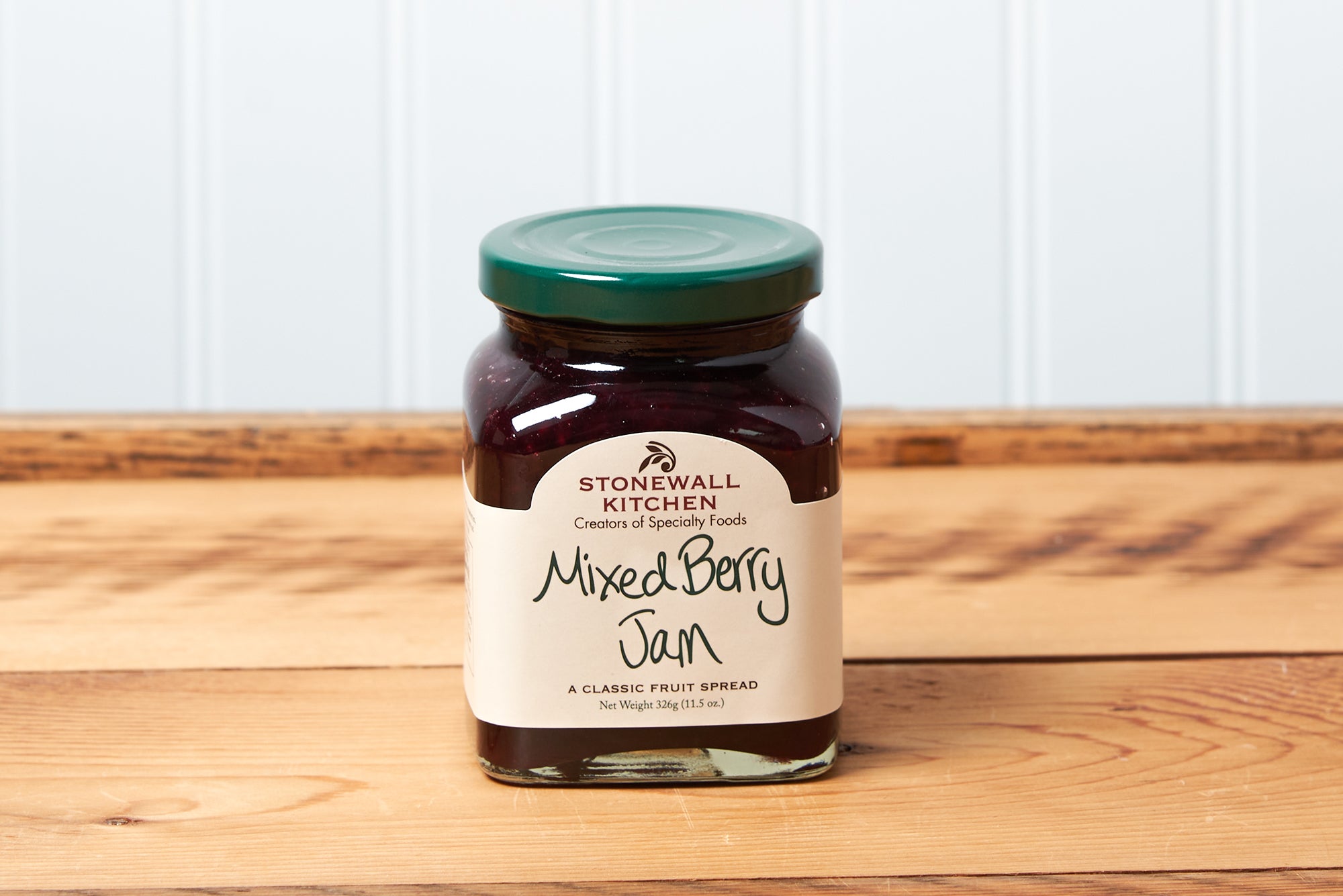 A jar of Stonewall Kitchen Mixed Berry Jam sits on a brown wooden table.