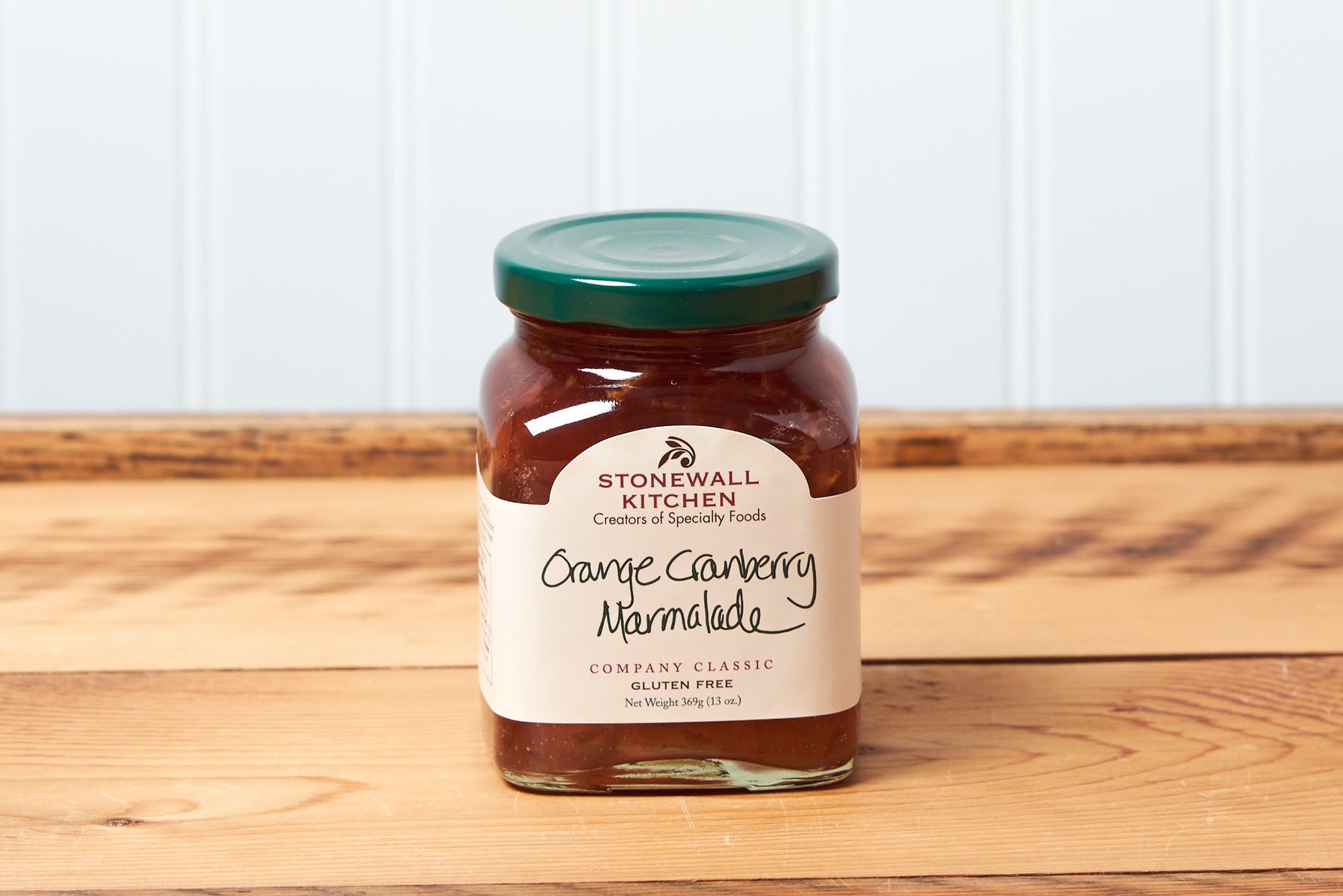 A jar of Stonewall Kitchen Orange Cranberry Marmalade sits on a brown wooden table.