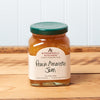 A jar of Stonewall Kitchen Peach Amaretto Jam sits on a brown wooden table.