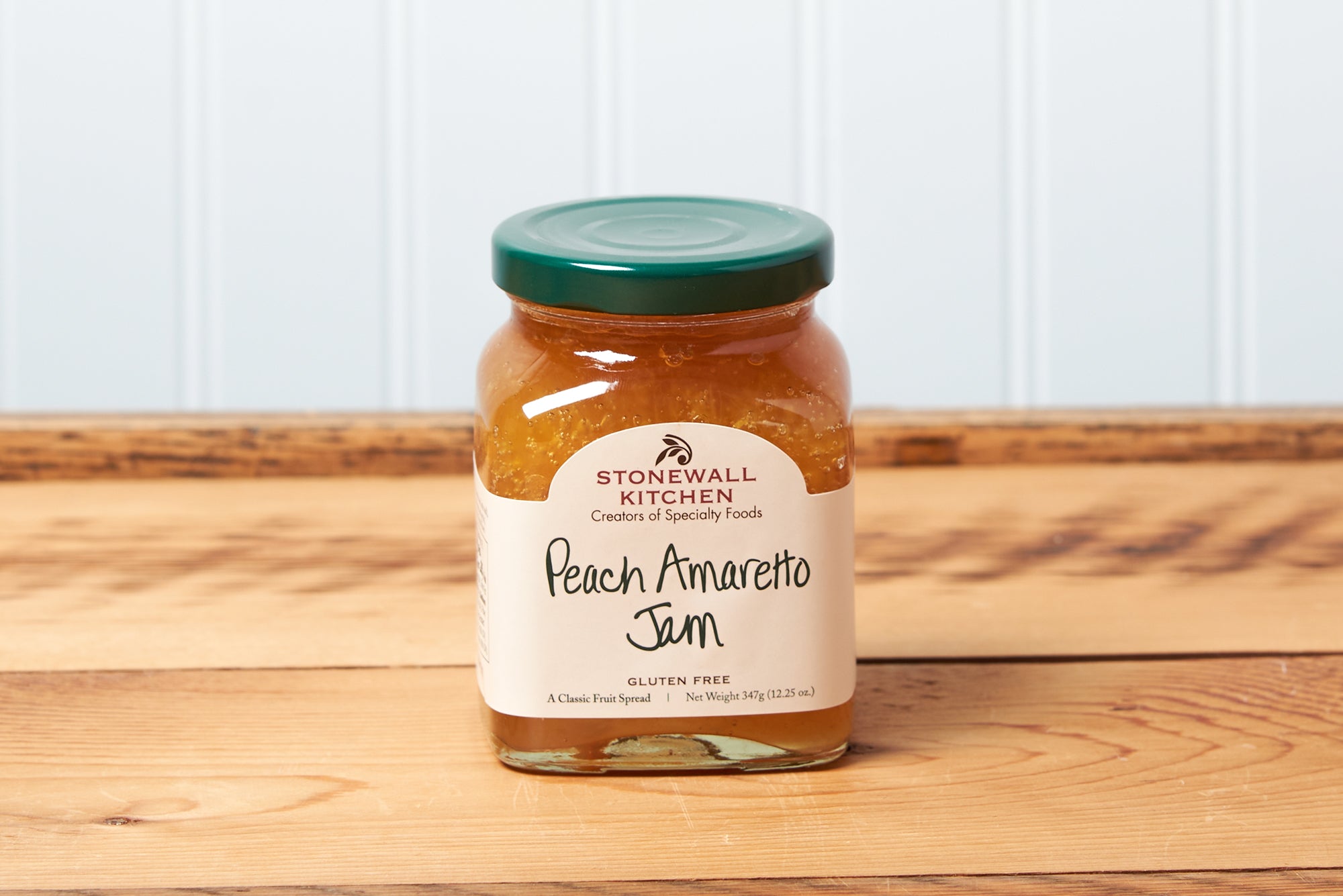 A jar of Stonewall Kitchen Peach Amaretto Jam sits on a brown wooden table.