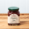A jar of Stonewall Kitchen Strawberry Jam sits on a brown wooden table.