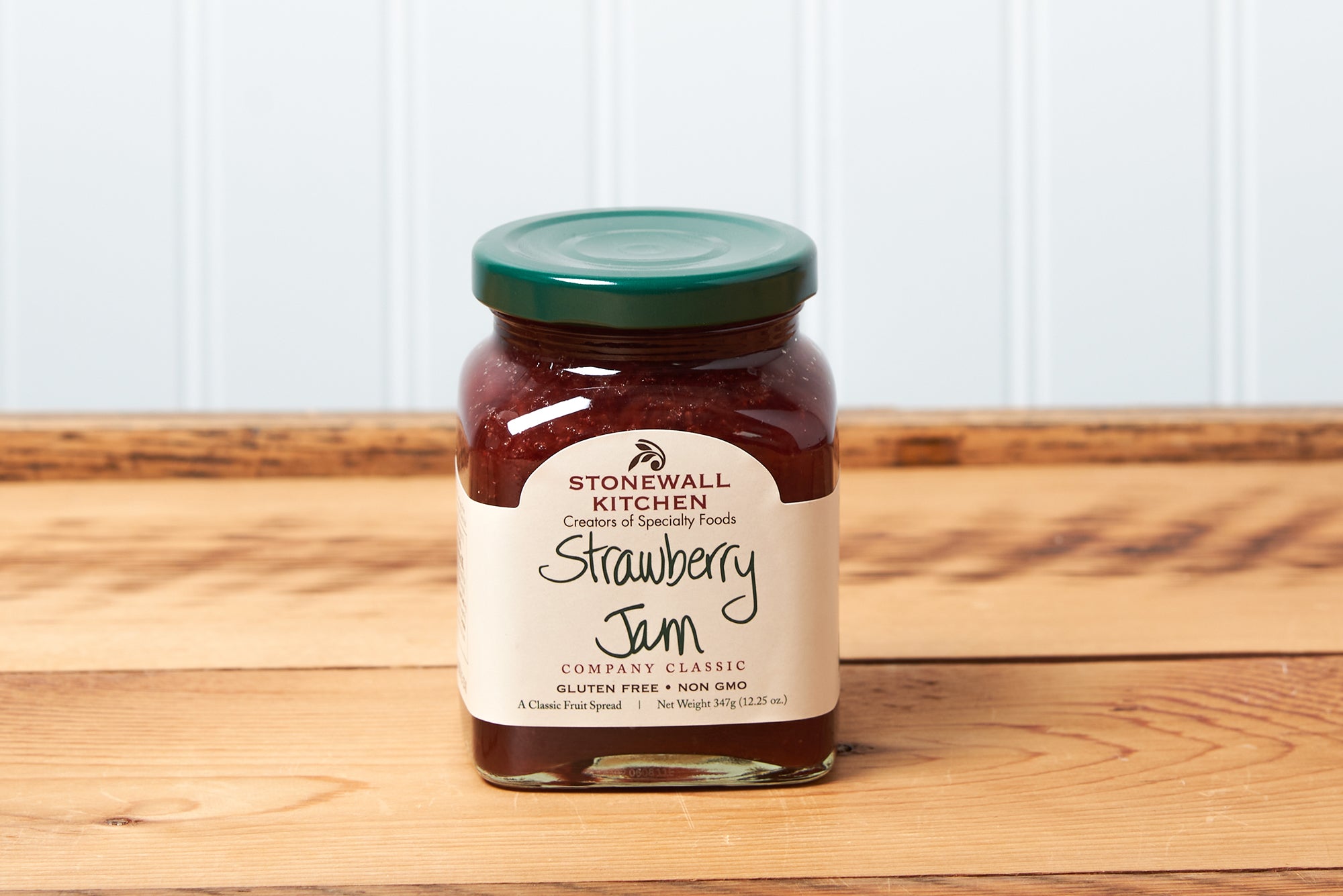 A jar of Stonewall Kitchen Strawberry Jam sits on a brown wooden table.