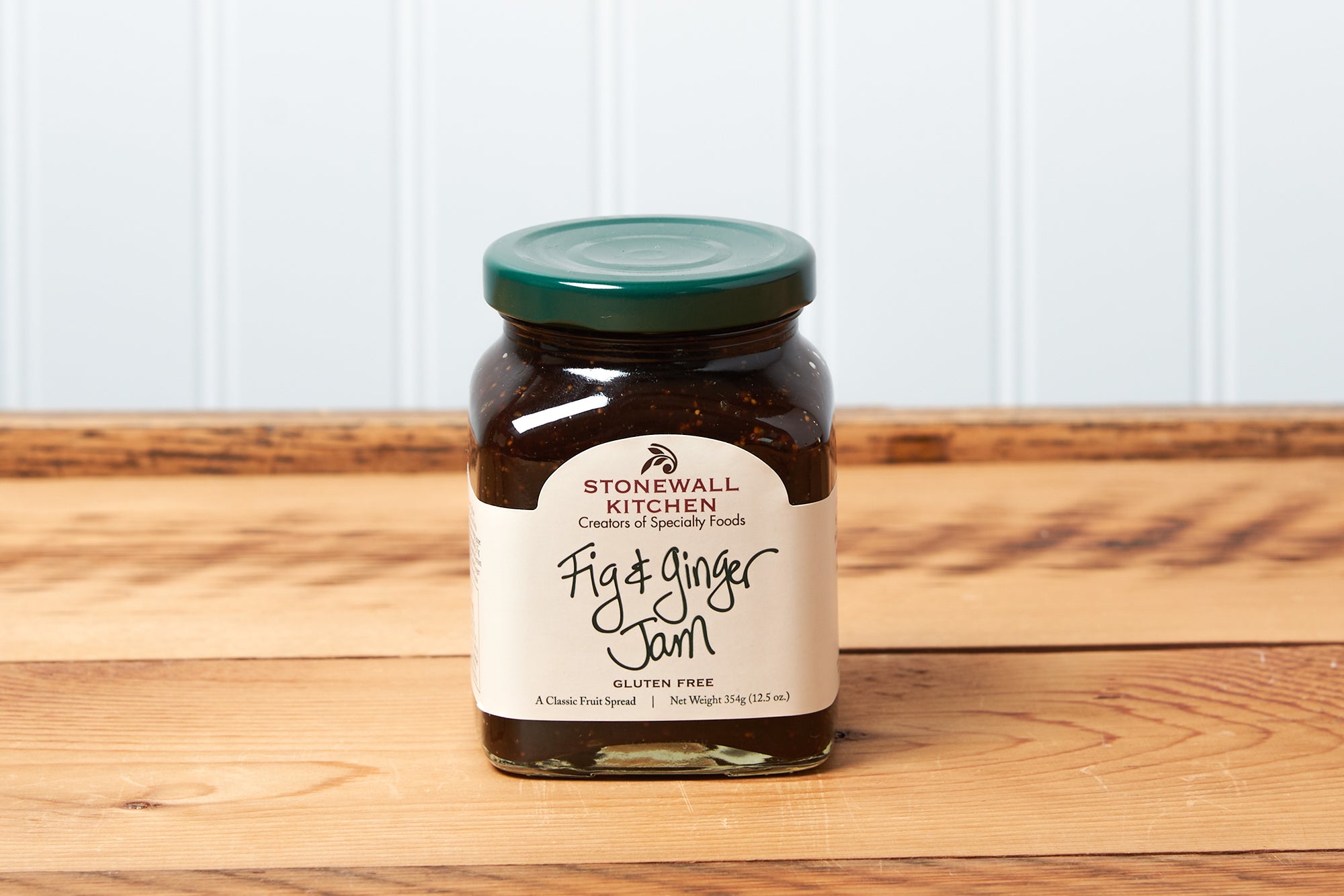 A jar of Stonewall Kitchen Fig & Ginger Jam sits on a brown wooden table.