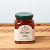 A jar of Stonewall Kitchen Hot Pepper Jelly sits on a brown wooden table.