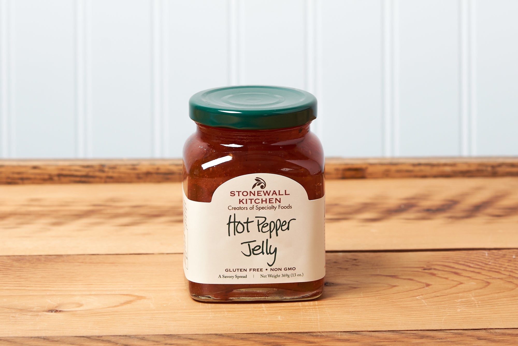 A jar of Stonewall Kitchen Hot Pepper Jelly sits on a brown wooden table.