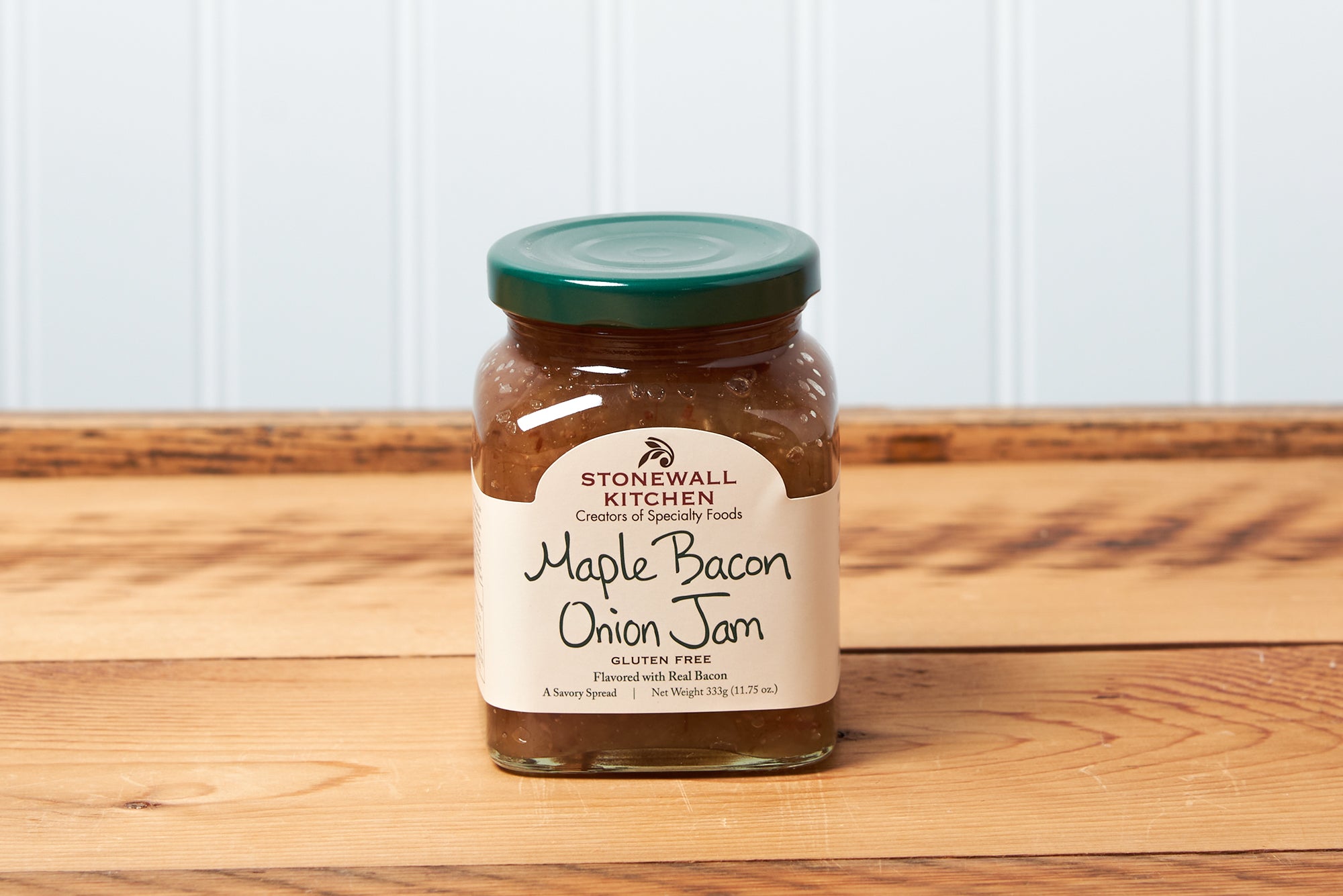A jar of Stonewall Kitchen Maple Bacon Onion Jam sits on a brown wooden table.