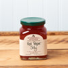A jar of Stonewall Kitchen Red Pepper Jelly sits on a brown wooden table.