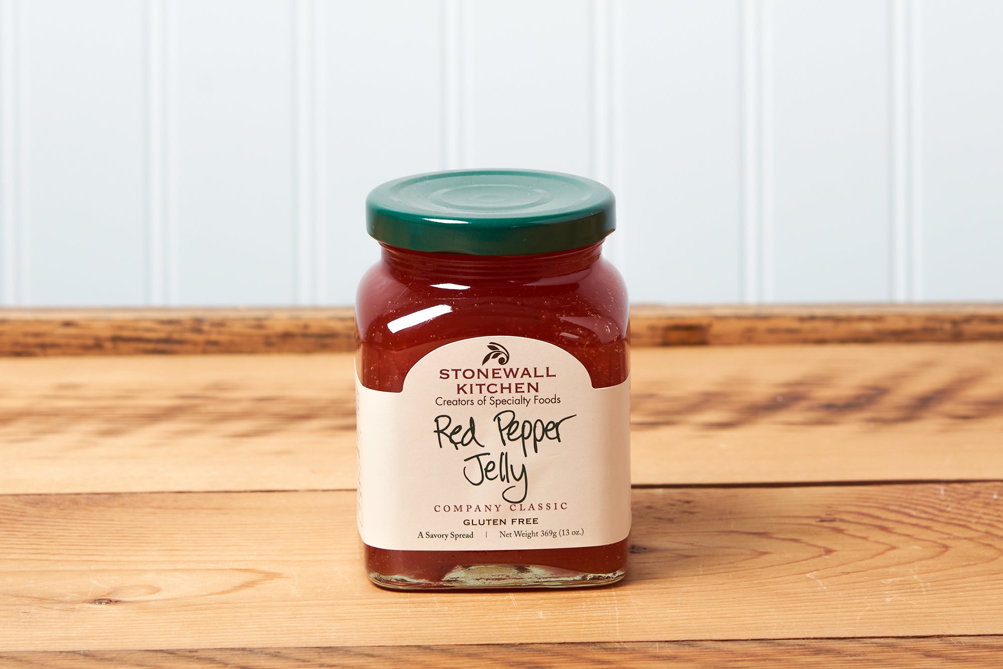A jar of Stonewall Kitchen Red Pepper Jelly sits on a brown wooden table.