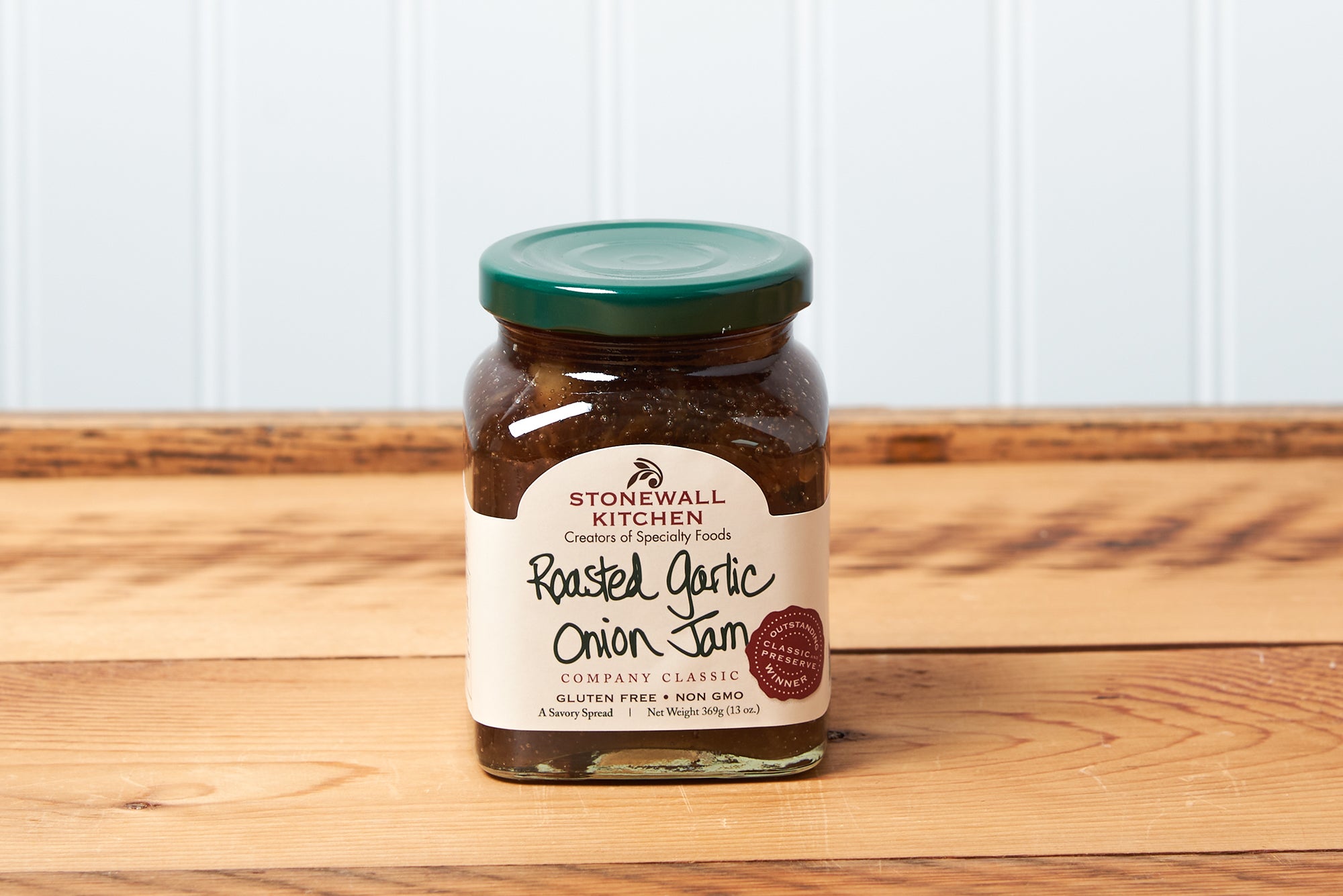 A jar of Stonewall Kitchen Roasted Garlic Onion Jam sits on a brown wooden table.