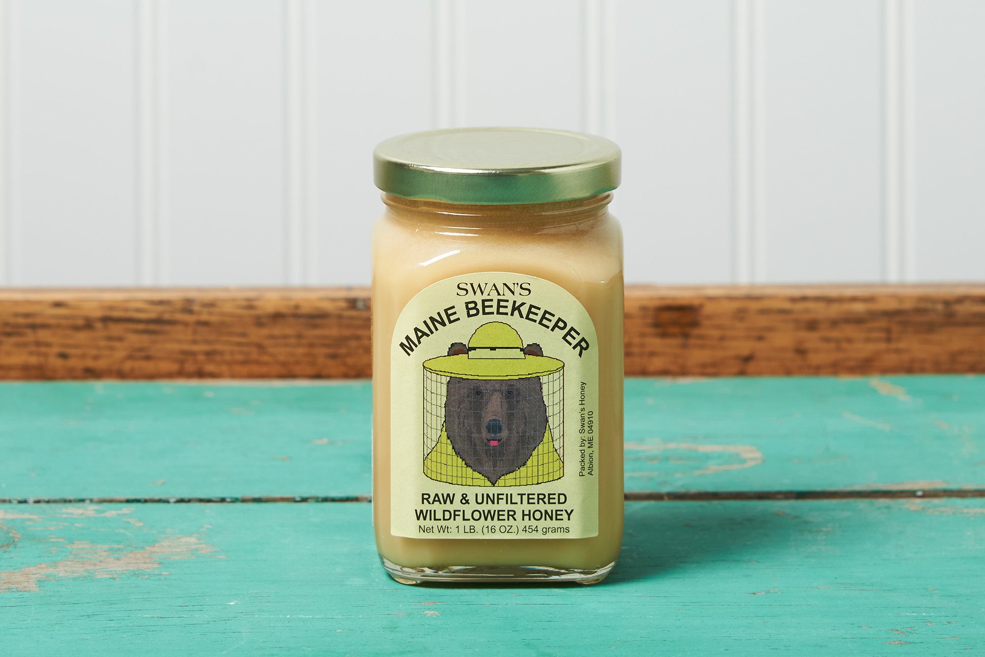 A jar of Swan's Raw Wildflower Honey sits on a turquoise wooden table.