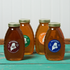 An assortment of four jars of Swan's Honey sits on a turquoise wooden table. the assortment includes the following honeys: Wild Raspberry, Wildflower, Orange Blossom, and Wild Blueberry