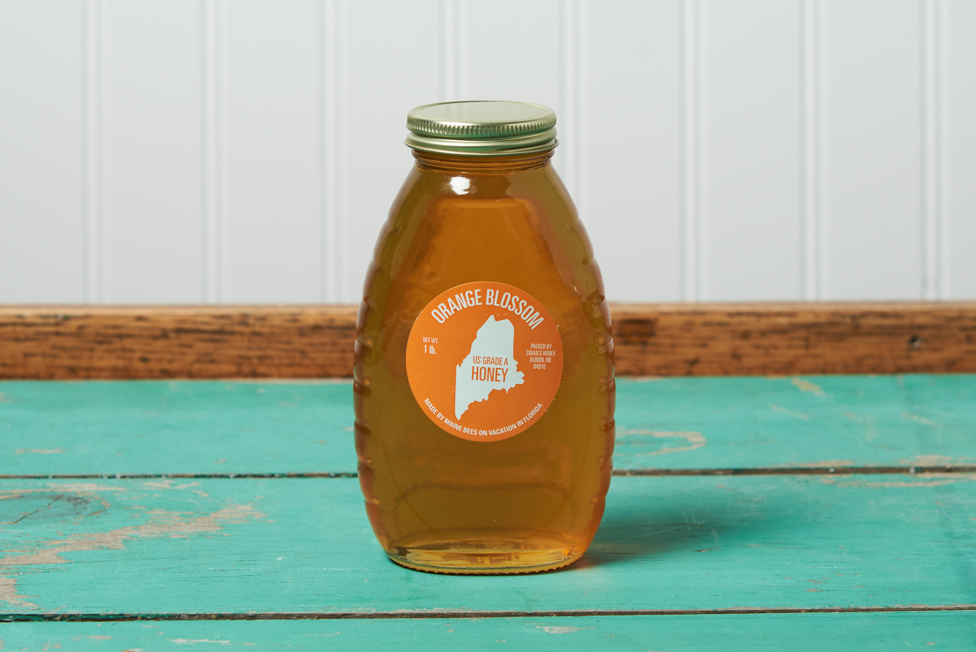 A jar of Swan's Orange Blossom Honey sits on a turquoise wooden table.