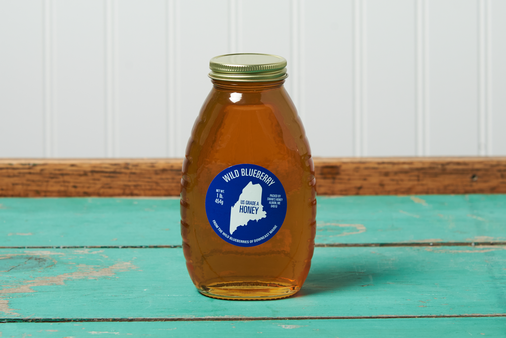 A jar of Swan's Wild Blueberry Honey sits on a turquoise wooden table.