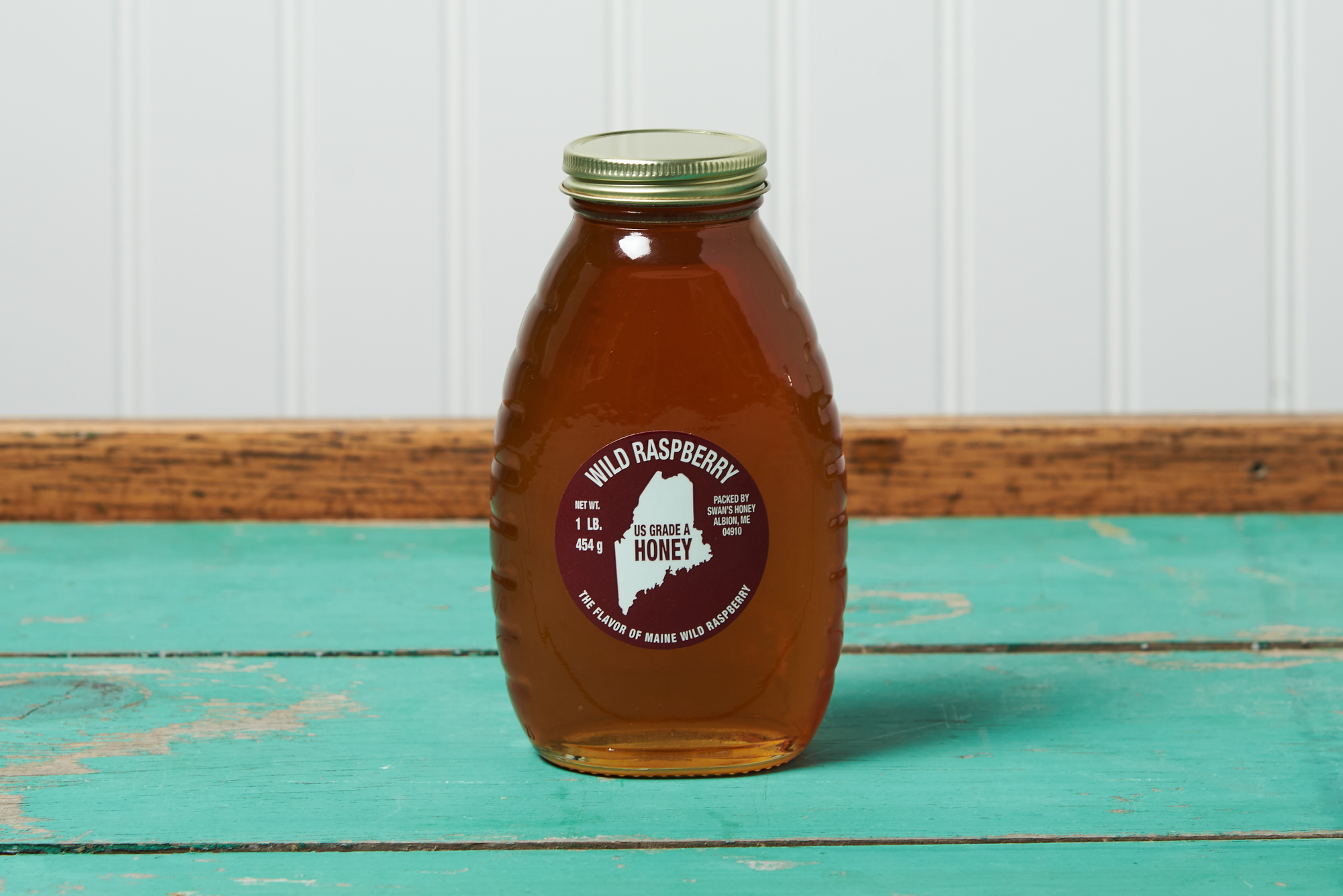 A jar of Swan's Raspberry Honey sits on a turquoise wooden table.