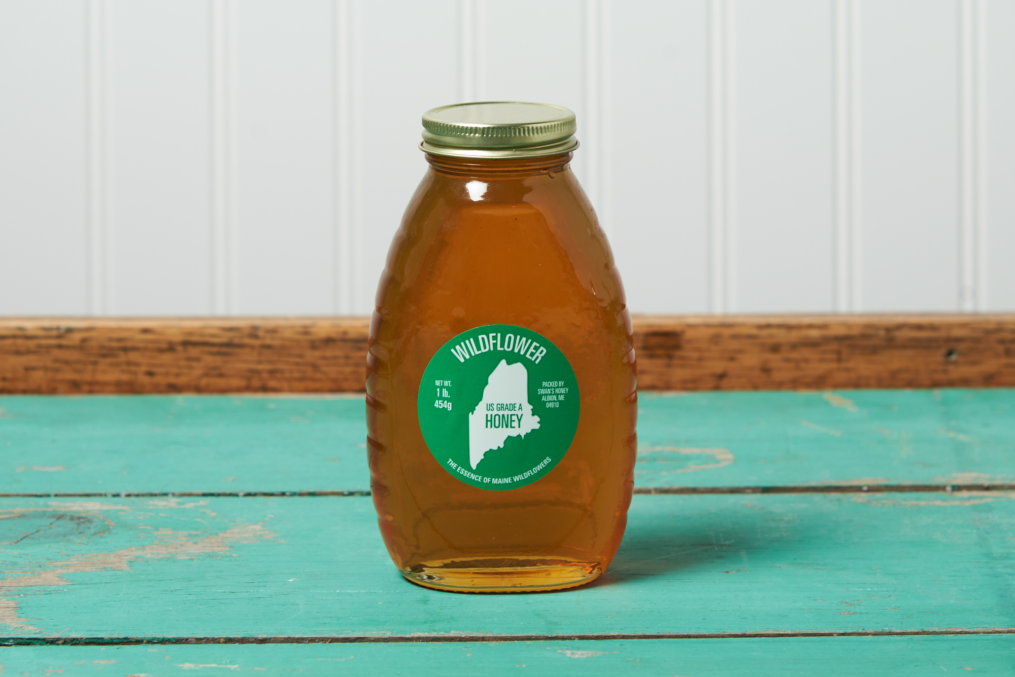 A jar of Swan's Wildflower Honey sits on a turquoise wooden table.