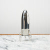 A cocktail shaker shaped like a rocket sits on a marble countertop.