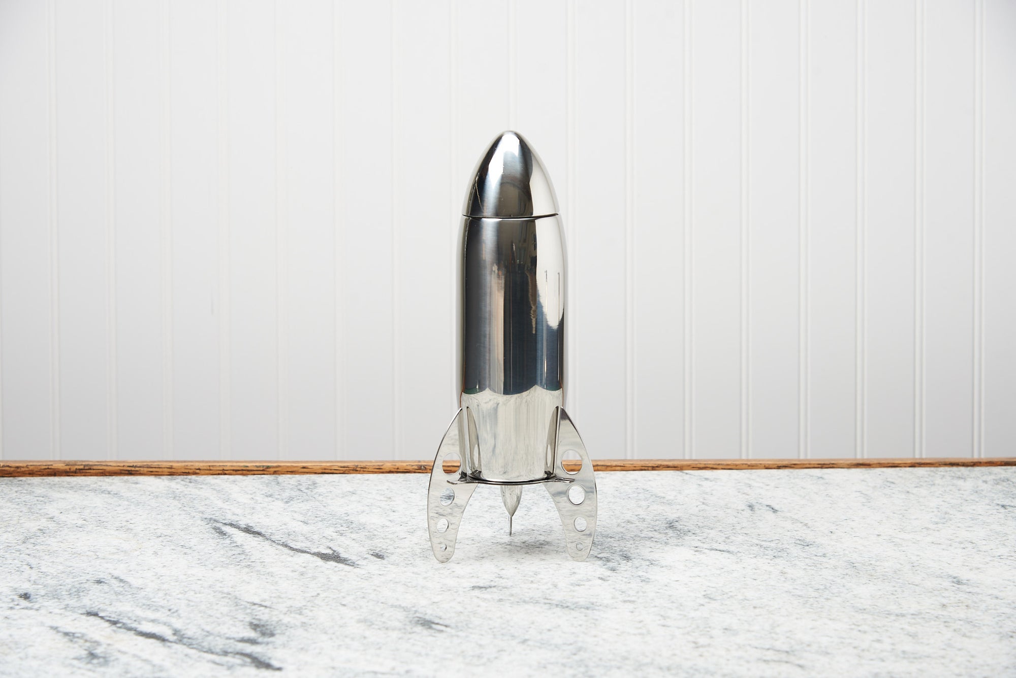 A cocktail shaker shaped like a rocket sits on a marble countertop.