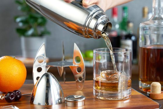 A cocktail is poured from a cocktail shaker into a rocks glass.