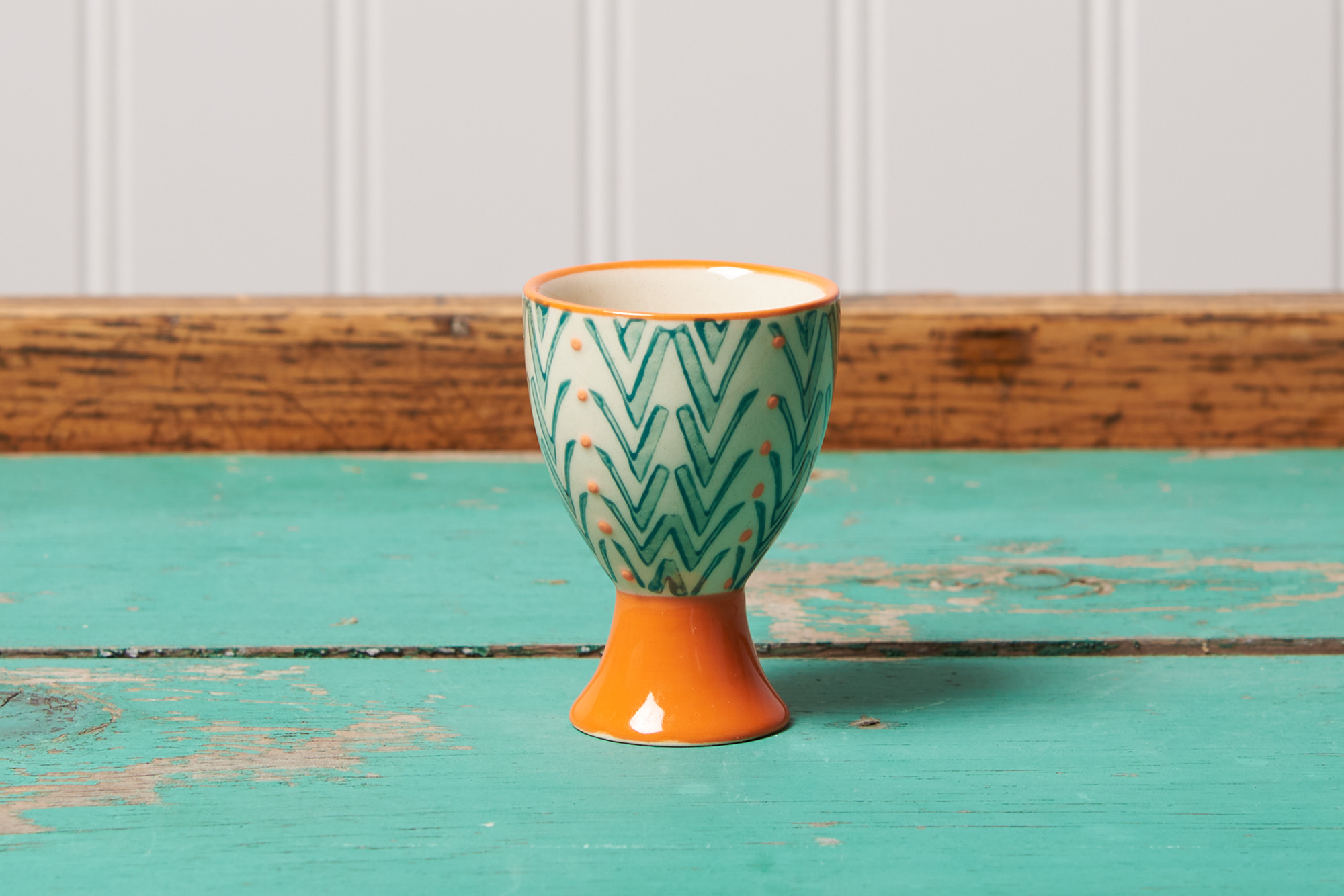 A green and yellow Tranquillo Egg Cup sits on a turquoise table.