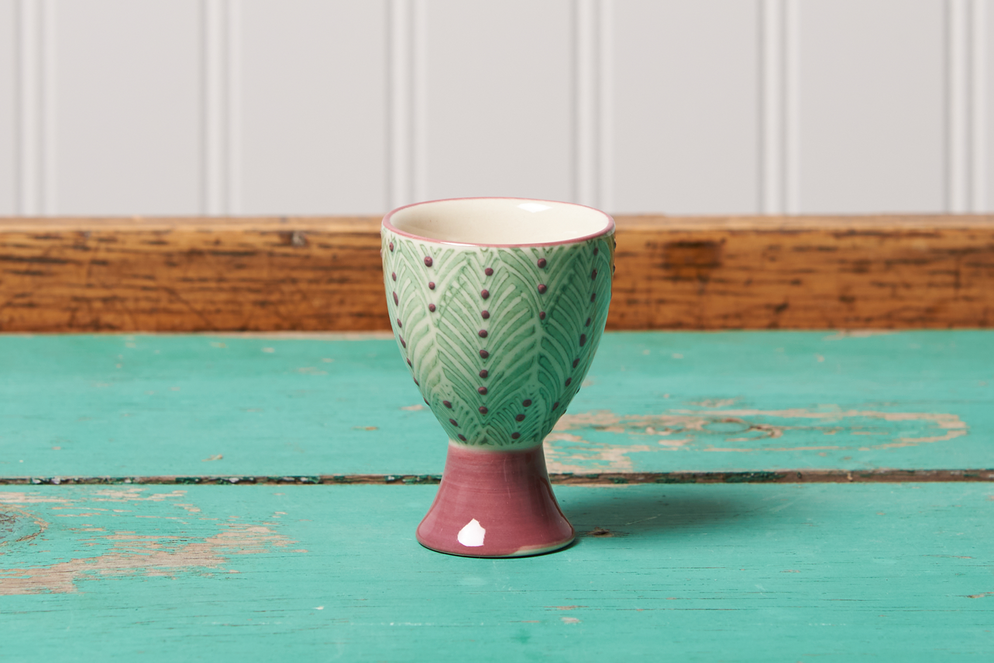 A purple dotted green Tranquillo Egg Cup sits on a turquoise table.