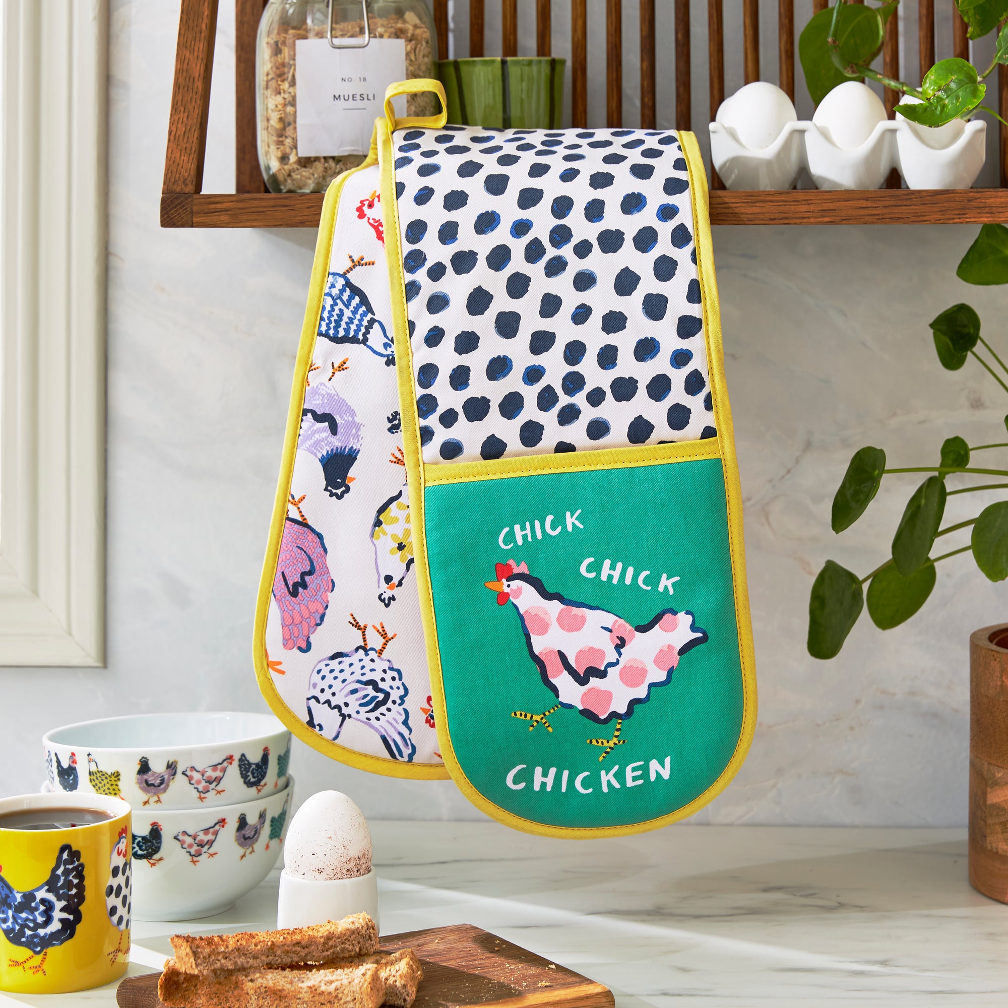 An Ulster Weavers Double Oven Mitt in the Chick Chicken pattern hangs over a kitchen countertop.