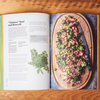 The cookbook 'Six Seasons: A New Way with Vegetables' sits open on a wooden table. The open page is a recipe and photo for "Chinese" Beef and Broccoli.