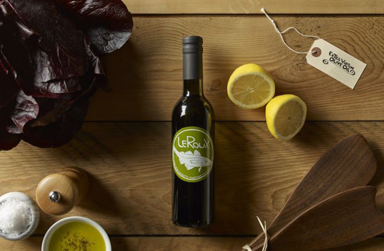 Olive oil bottle on wooden surface with lemons, salt, and fresh herbs