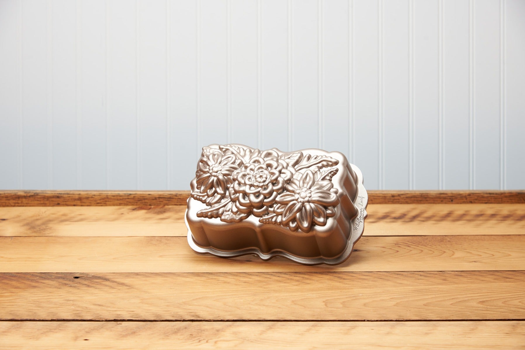 Embossed flower design metal cake pan on wooden table against blue wall