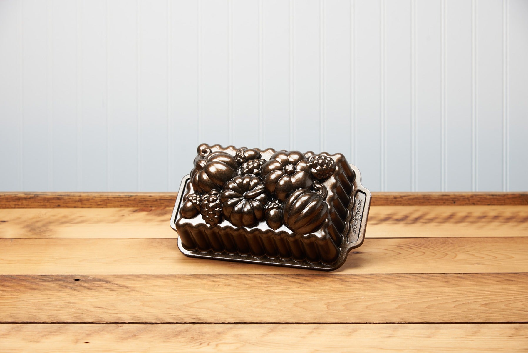 Bronze pumpkin-shaped baking pan on wooden table against a blue backdrop