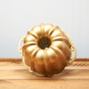 Golden bundt cake pan on wooden countertop with blue background
