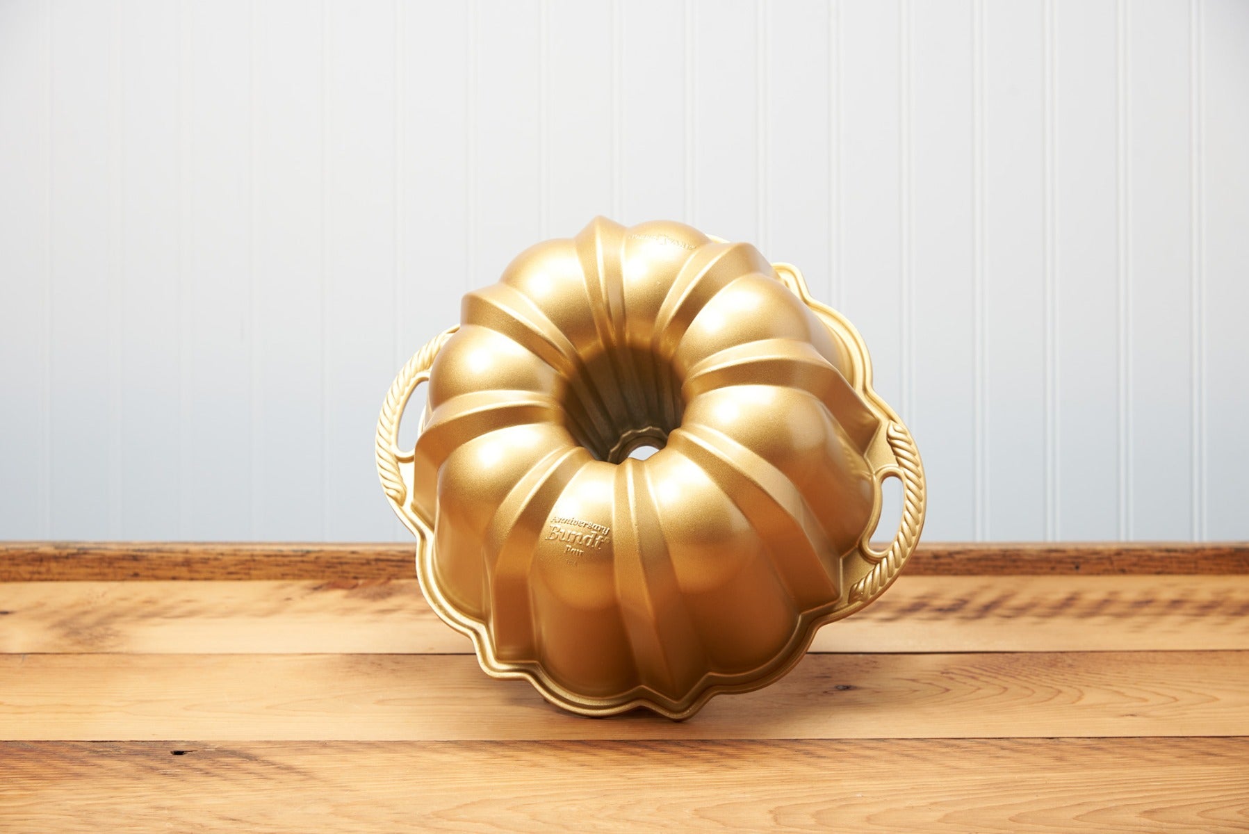 Golden bundt cake pan on wooden countertop with blue background