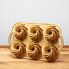 Gold bundt cake pan with swirl designs on a wooden table against blue background